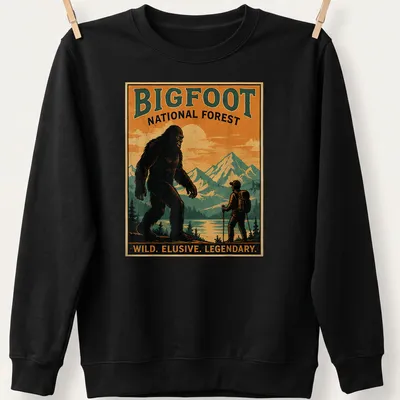Vintage poster style Bigfoot t-shirt with bold text and forest imagery — printed on a unisex sweatshirt
