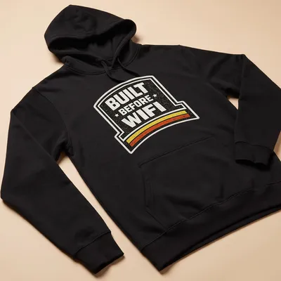 Retro humor t-shirt with 'BUILT BEFORE WIFI' in a badge design — printed on a unisex hoodie