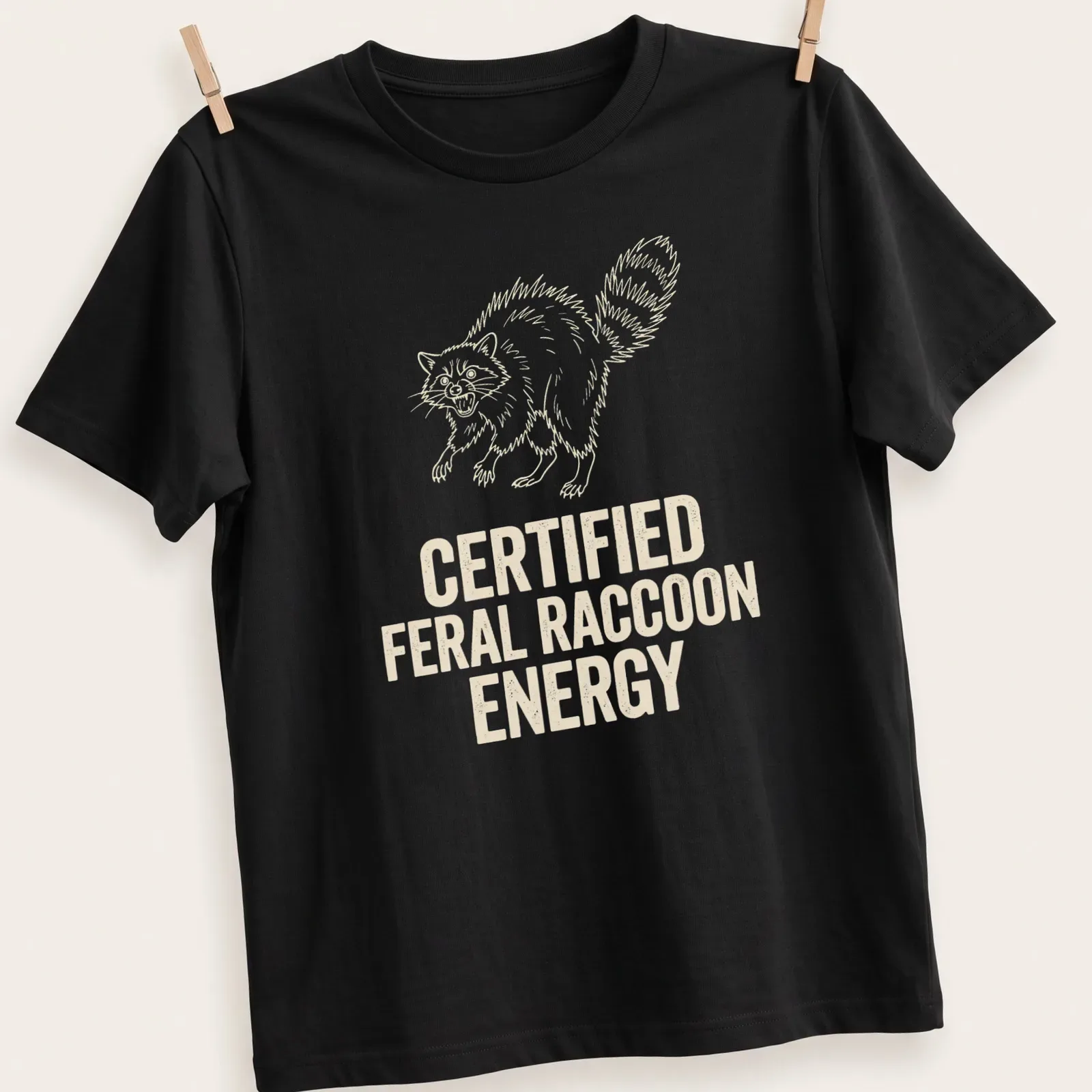 Line-art design of a feral raccoon with text declaring 'Certified Feral Raccoon Energy' — printed on a unisex t-shirt