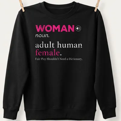 Bold typography design stating 'WOMAN noun. adult human female. Fair Play Shouldn't Need a Dictionary.' — printed on a unisex sweatshirt