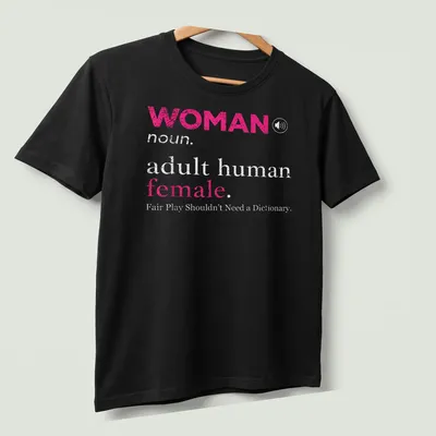 Bold typography design stating 'WOMAN noun. adult human female. Fair Play Shouldn't Need a Dictionary.' — printed on a unisex t-shirt (angled view)