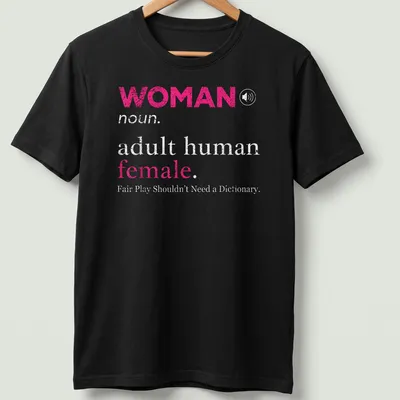 Bold typography design stating 'WOMAN noun. adult human female. Fair Play Shouldn't Need a Dictionary.' — printed on a unisex t-shirt