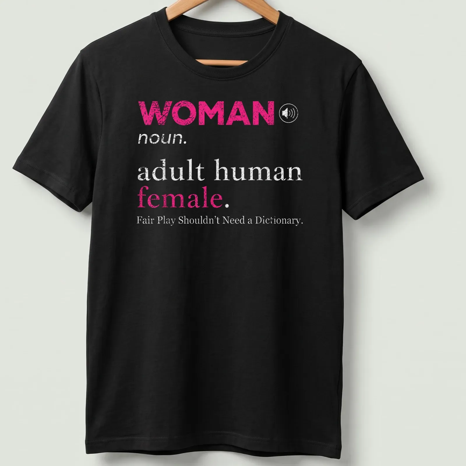 Bold typography design stating 'WOMAN noun. adult human female. Fair Play Shouldn't Need a Dictionary.' — printed on a unisex t-shirt