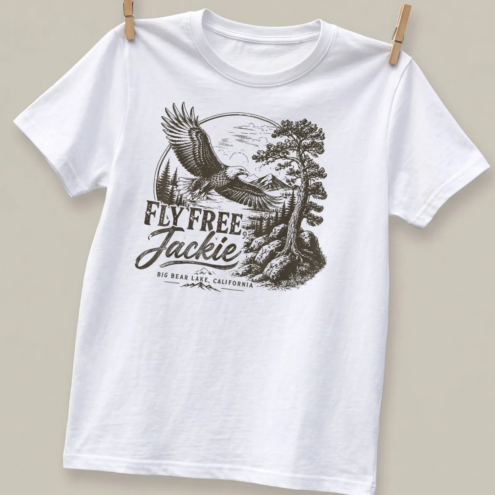 Vintage eagle graphic with text reading 'FLY FREE, Jackie BIG BEAR LAKE, CALIFORNIA' in black, white, and gray — printed on a unisex t-shirt