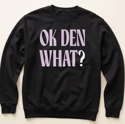 Light purple t-shirt with bold printed text saying OK DEN WHAT — printed on a unisex sweatshirt