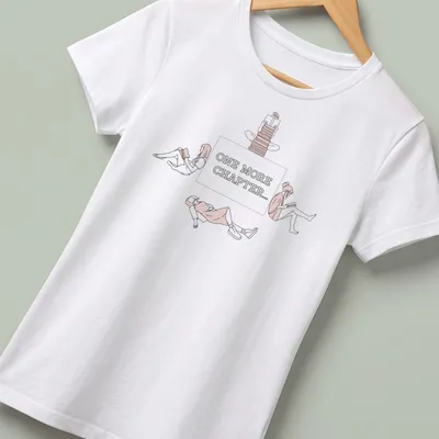 Line-art graphic tee showing the text 'One More Chapter...' with book-themed illustrations — printed on a women's shirt