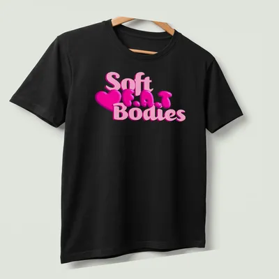 Playful pink heart design with bubble lettering reading 'Soft F.A.T Bodies' — printed on a unisex t-shirt (angled view)