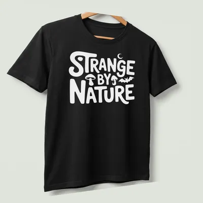 Colorful nature scene t-shirt featuring the text 'Strange By Nature' above an illustration. — printed on a unisex t-shirt (angled view)