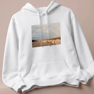 Illustration of a rainbow over a beach landscape with blue and green hues. — printed on a unisex hoodie