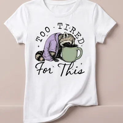 Vintage illustration of a raccoon face down in a coffee cup with playful text — printed on a women's shirt