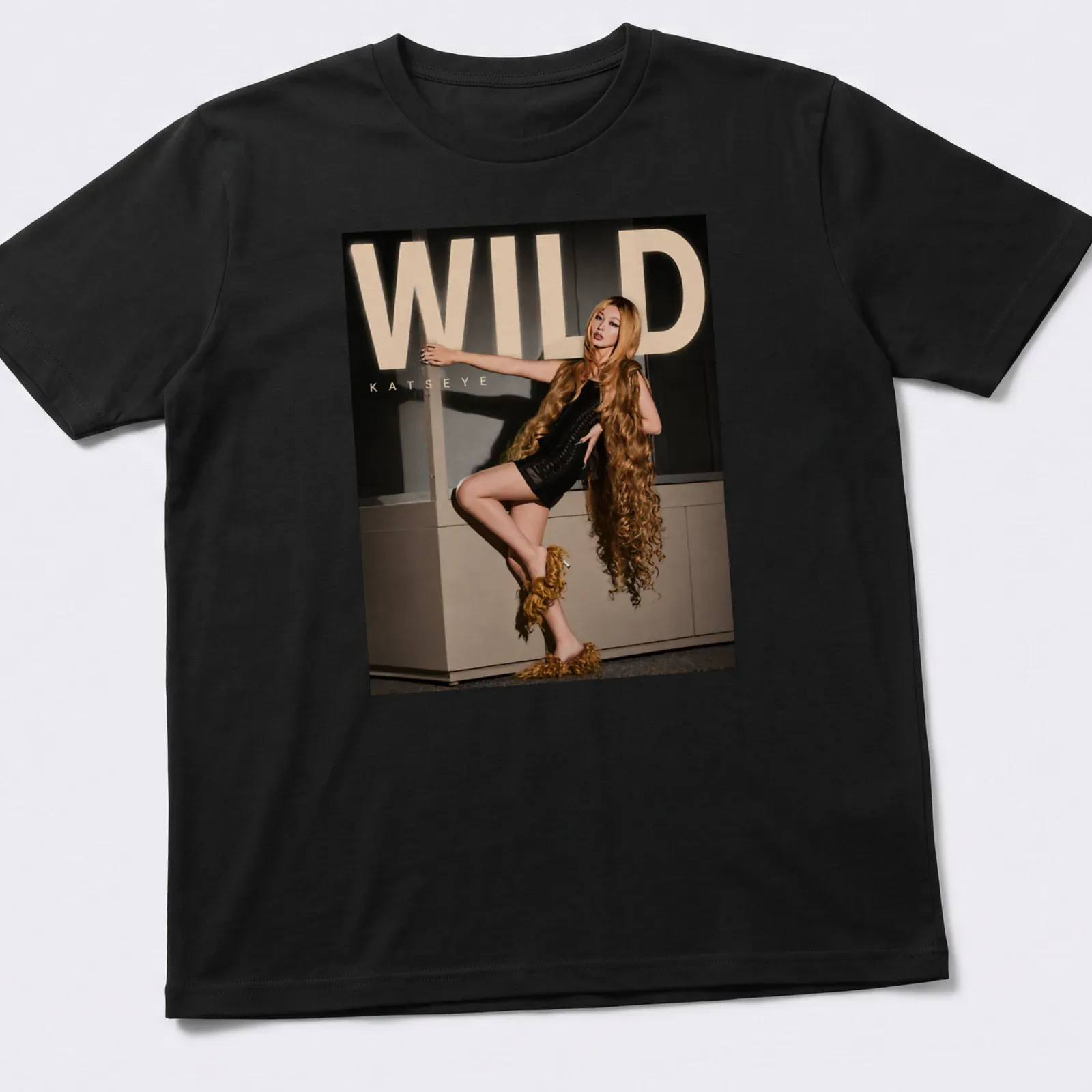 Bold WILD Katseye text above an illustration of a fashion model in gold and black — printed on a unisex t-shirt